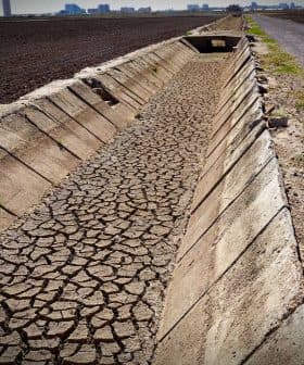 Cracked dry irrigation canal running alongside a gravel road in an agricultural area. - Olive Oil Times