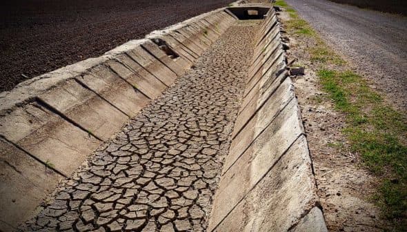 Cracked dry irrigation canal running alongside a gravel road in an agricultural area. - Olive Oil Times