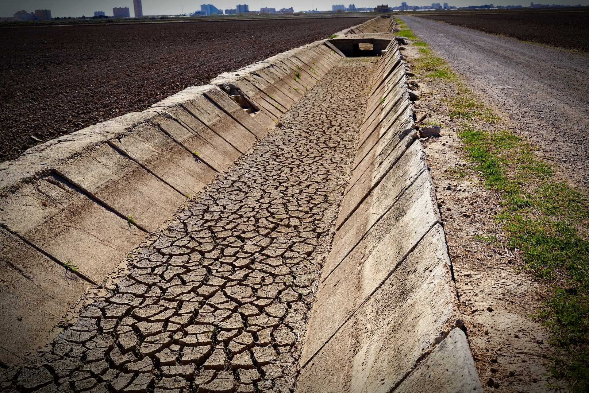 Cracked dry irrigation canal running alongside a gravel road in an agricultural area. - Olive Oil Times