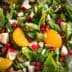 A bowl of mixed green salad featuring spinach, apple pieces, orange segments, pomegranate seeds, and sliced almonds. - Olive Oil Times