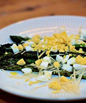 Plate of cooked asparagus topped with chopped egg and grated cheese. - Olive Oil Times
