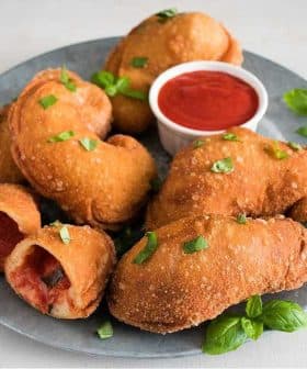 A plate of fried dough pieces garnished with green herbs and served with a small bowl of tomato sauce. - Olive Oil Times