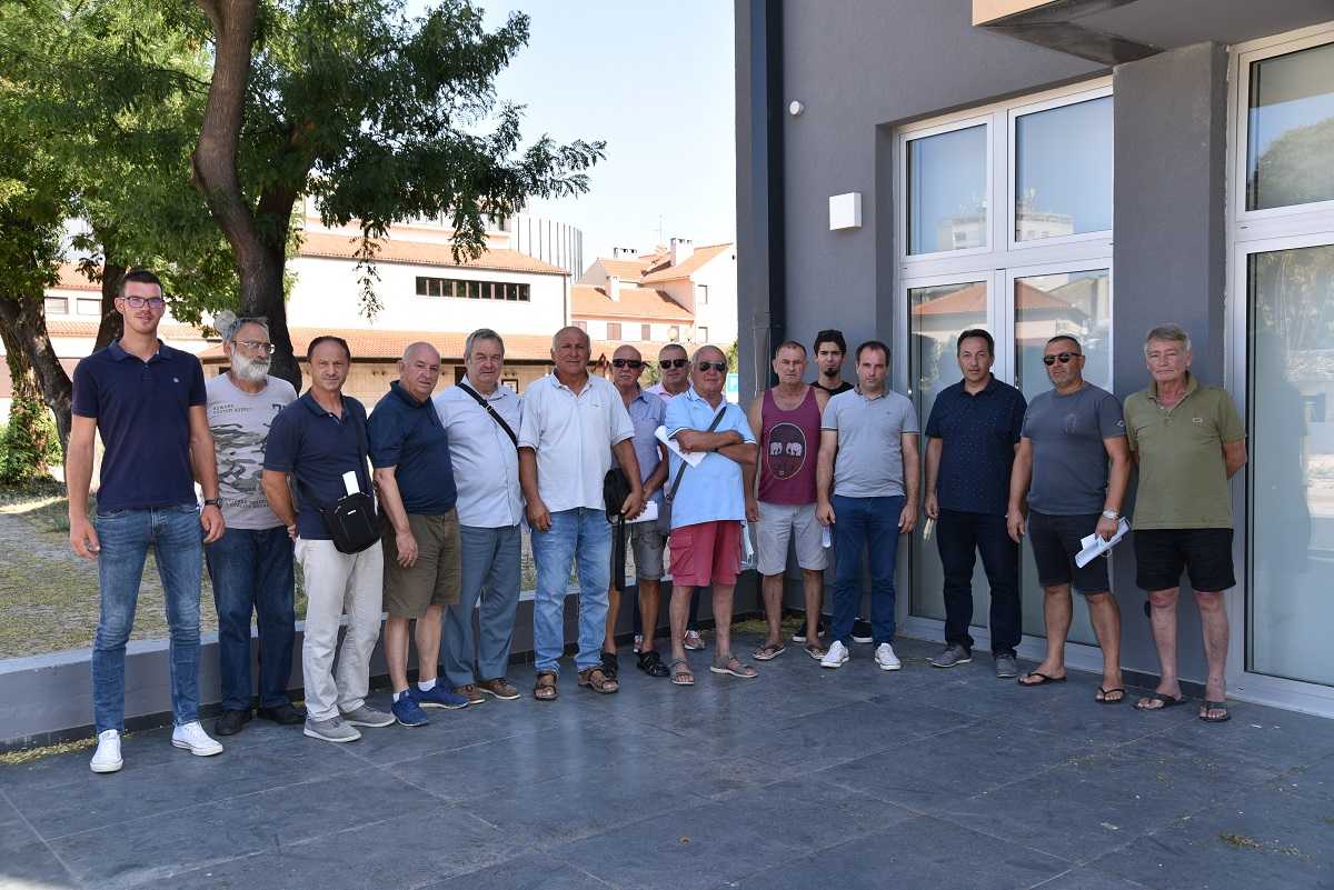 A group of individuals standing together in a line outside a building, some wearing sunglasses and casual clothing. - Olive Oil Times