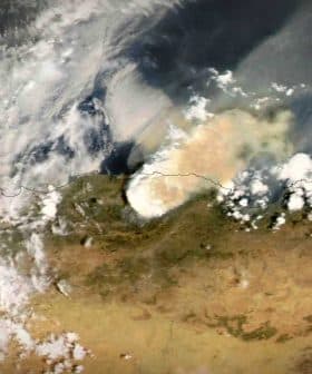 Satellite view showing smoke rising from a wildfire in a landscape with clouds and terrain visible. - Olive Oil Times