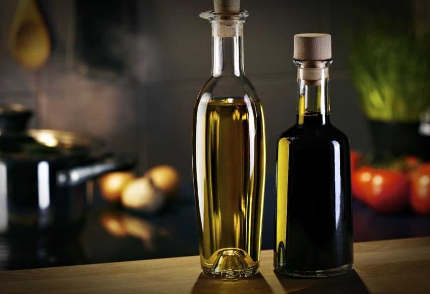 Two glass bottles containing olive oil, one with a light golden liquid and the other with a dark liquid, placed on a wooden surface. - Olive Oil Times