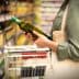 Individual holding a green bottle of olive oil while shopping in a grocery store aisle. - Olive Oil Times