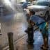 A child in swim trunks leaning against a fire hydrant with water spraying out onto the street. - Olive Oil Times