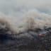 Thick smoke billowing from a wildfire with visible flames in a mountainous region. - Olive Oil Times