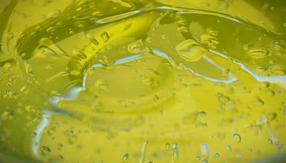 Close-up view of olive oil with bubbles in a glass container. - Olive Oil Times