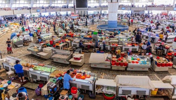A bustling market filled with vendors and customers, showcasing various stalls and products in a large indoor space. - Olive Oil Times