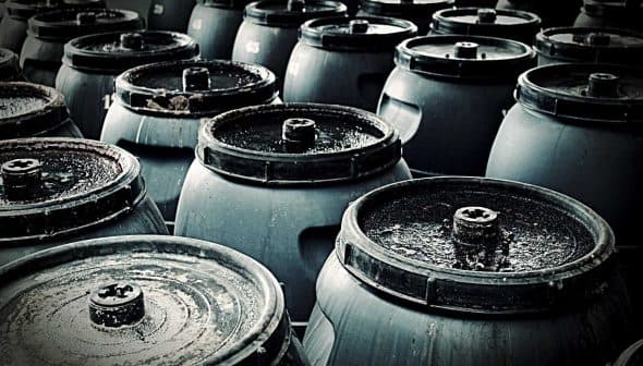 A group of dark storage barrels arranged closely together, showing their tops and lids. - Olive Oil Times