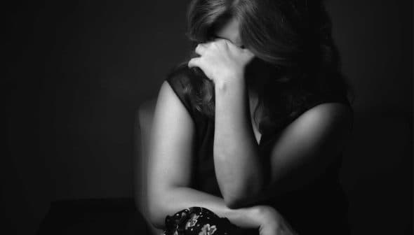 A woman with long hair sitting with her hand covering her face in a black and white photograph. - Olive Oil Times