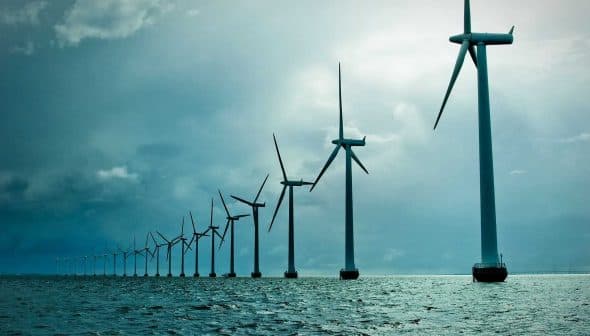 Row of offshore wind turbines standing in the ocean under a cloudy sky. - Olive Oil Times