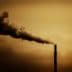 Smoke billowing from the top of an industrial smokestack against a cloudy sky. - Olive Oil Times