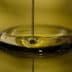 Stream of olive oil pouring into a circular pool of oil, creating ripples on the surface. - Olive Oil Times