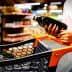 Individual holding a bottle of olive oil while standing next to a shopping cart in a store. - Olive Oil Times