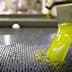 Freshly extracted olive oil flowing from a spout into a collection container during the production process. - Olive Oil Times