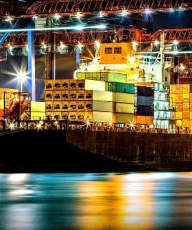 Cargo ship docked at a port, loaded with colorful shipping containers at night. - Olive Oil Times