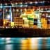 Cargo ship docked at a port, loaded with colorful shipping containers at night. - Olive Oil Times