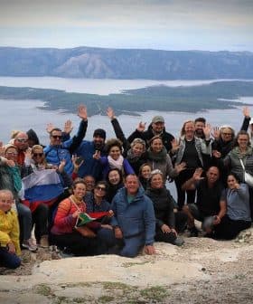 A large group of people posing together on a mountain with arms raised in celebration. - Olive Oil Times
