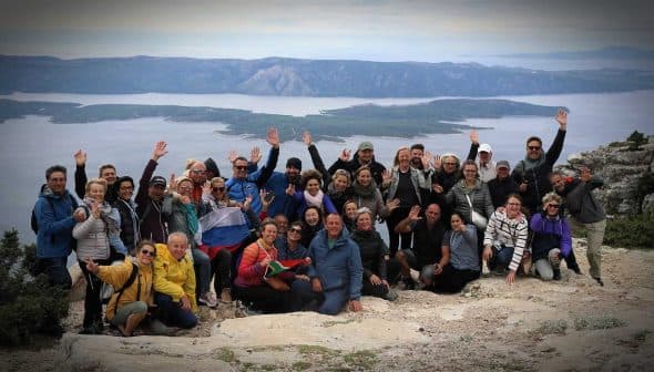 A large group of people posing together on a mountain with arms raised in celebration. - Olive Oil Times