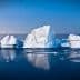 Icebergs floating in calm waters with a blue sky in the background during twilight. - Olive Oil Times