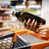 Individual holding a dark glass bottle of olive oil while standing next to a shopping cart. - Olive Oil Times