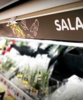 Sign labeled 'SALAD' in a grocery store aisle with various salad ingredients visible. - Olive Oil Times
