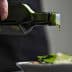 A person pouring olive oil from a dark green bottle onto a fresh salad in a white bowl. - Olive Oil Times