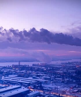 Industrial power plant with smoke rising from tall chimneys against a twilight sky. - Olive Oil Times