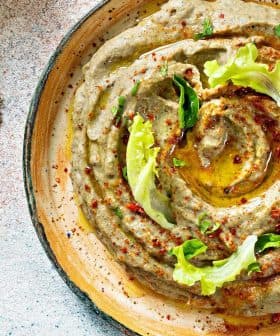 Bowl of hummus topped with olive oil, herbs, and spices, served with flatbread on the side. - Olive Oil Times