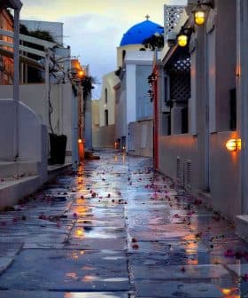 Narrow cobblestone alley with a blue dome building in the background and flower petals on the ground. - Olive Oil Times