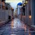Narrow cobblestone alley with a blue dome building in the background and flower petals on the ground. - Olive Oil Times