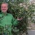 Man in a green jacket standing among olive branches with olives in hand. - Olive Oil Times