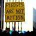 Yellow sign at a protest reading 'Pledges Are Not Action' held by an individual in a crowd. - Olive Oil Times