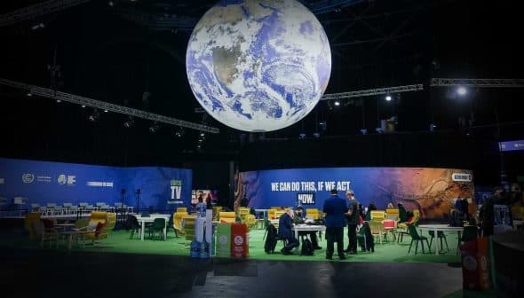 A large globe installation suspended from the ceiling in a conference venue with seating areas below. - Olive Oil Times