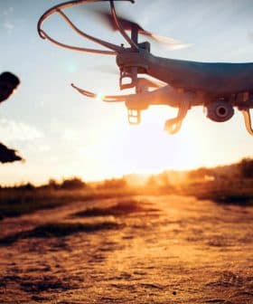 A drone flying in the foreground with a person operating it in the background during sunset. - Olive Oil Times