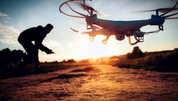 A drone flying in the foreground with a person operating it in the background during sunset. - Olive Oil Times