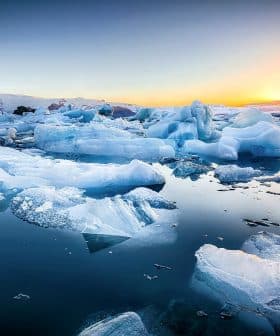 Icebergs of various shapes and sizes floating in calm water during sunset with a colorful sky. - Olive Oil Times