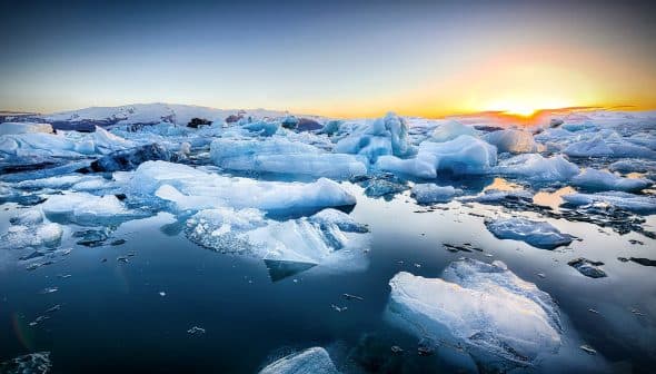 Icebergs of various shapes and sizes floating in calm water during sunset with a colorful sky. - Olive Oil Times