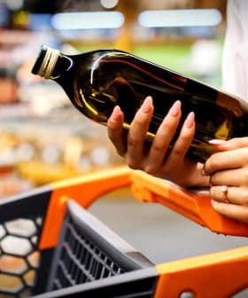 Person holding a bottle of olive oil while pushing a shopping cart in a store. - Olive Oil Times