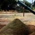 A pyramid-shaped mound of soil on a construction site with machinery in the background. - Olive Oil Times