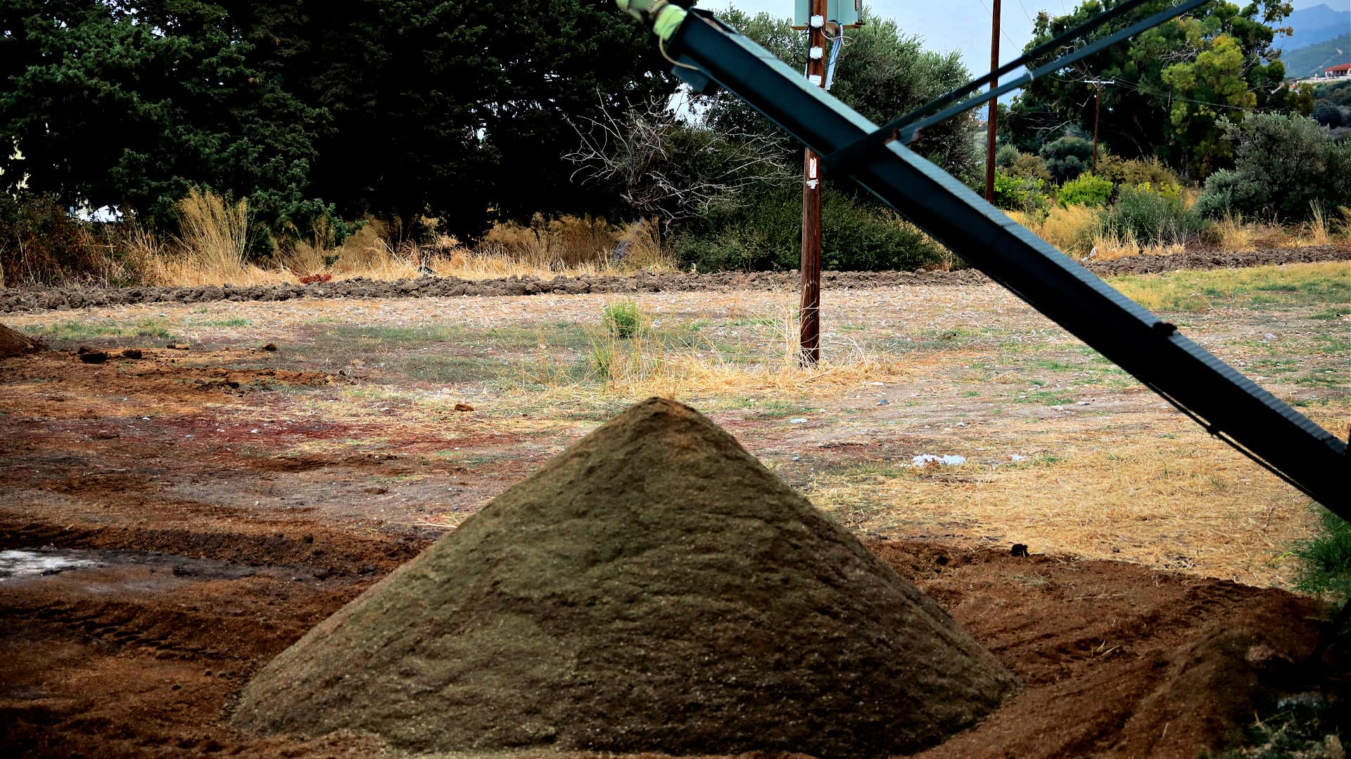 A pyramid-shaped mound of soil on a construction site with machinery in the background. - Olive Oil Times