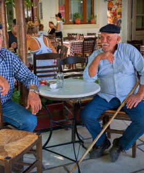 Two older men with hats sitting at a small round table in a café setting. - Olive Oil Times