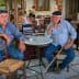 Two older men with hats sitting at a small round table in a café setting. - Olive Oil Times