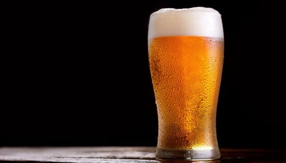 A glass of beer with foam on top, featuring condensation on the outside. - Olive Oil Times