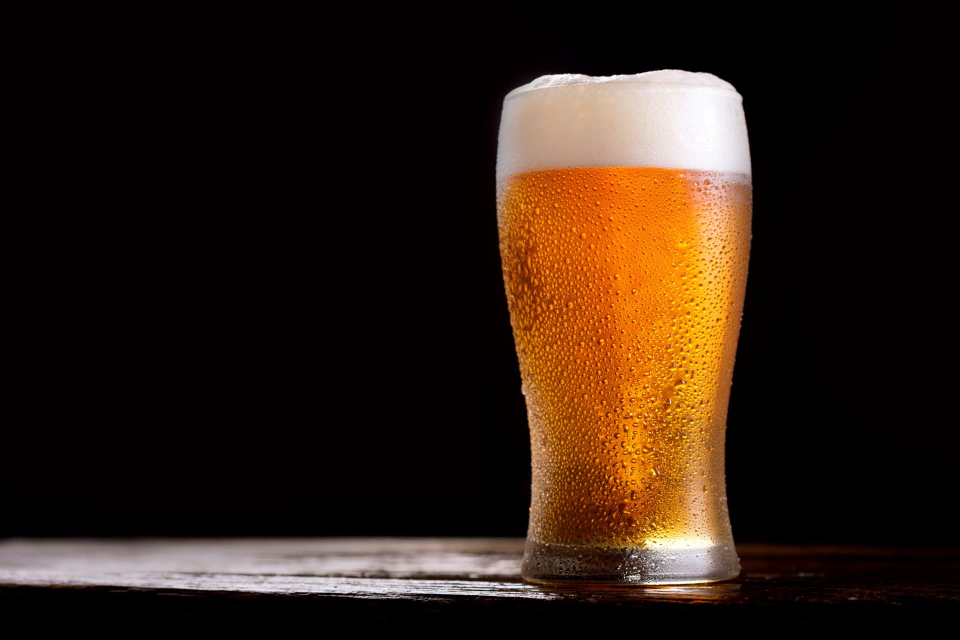 A glass of beer with foam on top, featuring condensation on the outside. - Olive Oil Times