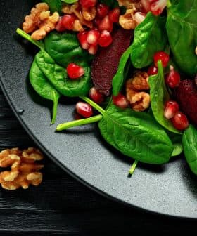 A black plate filled with spinach leaves, pomegranate seeds, and walnuts arranged together. - Olive Oil Times