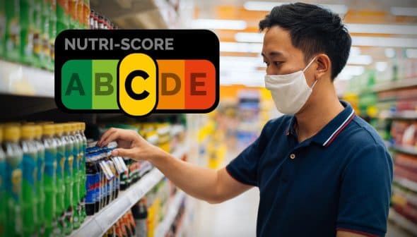 Man wearing a mask examining beverage labels on a supermarket shelf with a Nutri-Score graphic in the background. - Olive Oil Times