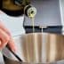 A person pouring olive oil from a bottle into a stainless steel mixing bowl. - Olive Oil Times